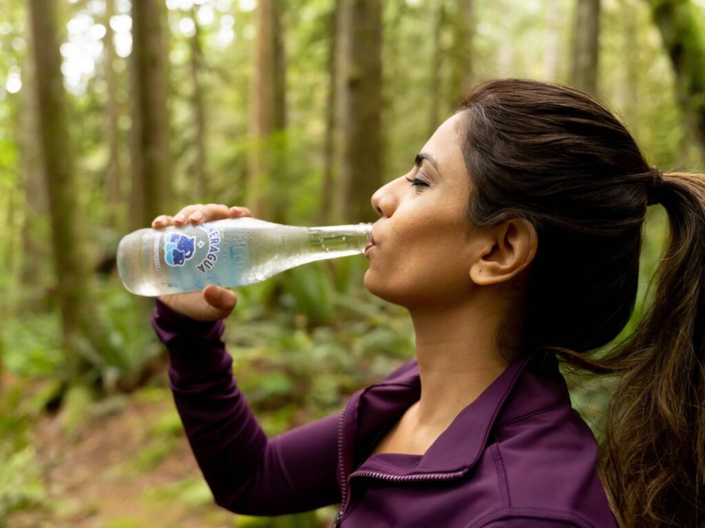 Vista lateral de uma mulher com agasalhos de corrida em uma trilha bebendo água