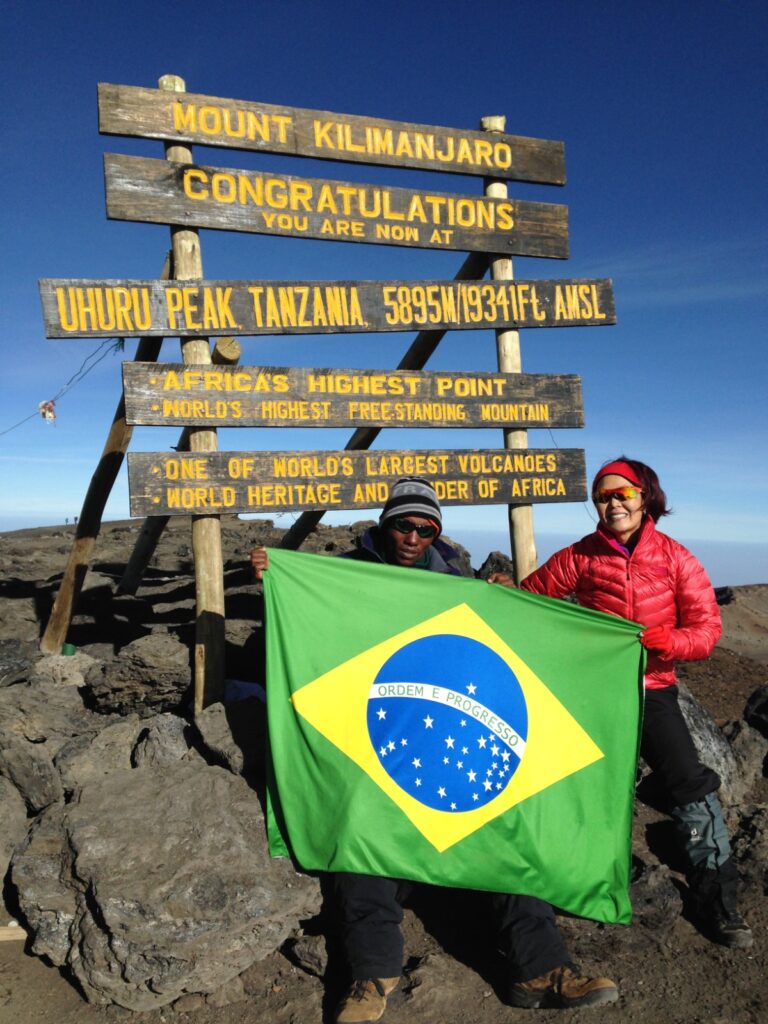 Vista de uma corredora em frente uma placa com a bandeira do Brasil na Meia Maratona do Kilimanjaro na africa.