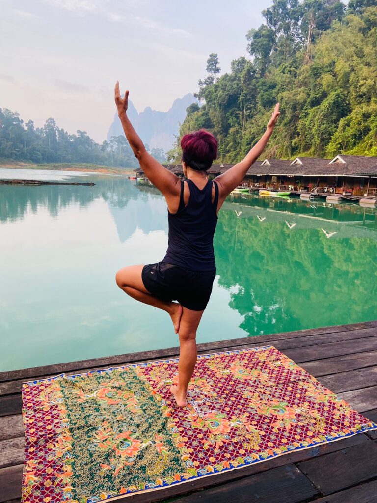 Vista de uma mulher de costas praticando yoga em frente a uma paisagem na Tailândia.