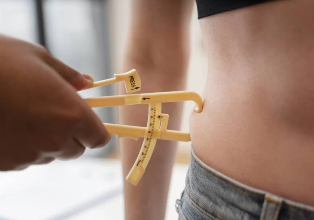 Visão aproximada de uma pessoa usando um adipômetro para medir a gordura de uma parte da barriga.